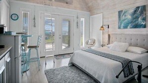 A bedroom with a bed, a desk, and a chair. There is a window with blinds, a painting on the wall, and a clock on the wall. - Spacious Crystal Beach Home | | Hot Tub | Walk to Beach | Sleeps 18 (Crystal Beach)