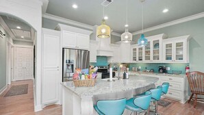 A modern kitchen with white cabinetry, a large island with bar stools, and pendant lighting. - Spacious Crystal Beach Home | | Hot Tub | Walk to Beach | Sleeps 18 (Crystal Beach)