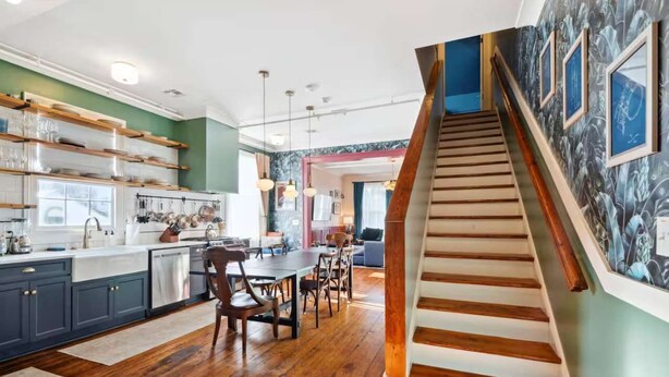 Una cocina moderna con piso de madera, un comedor con sillas y una escalera con barandilla de madera.