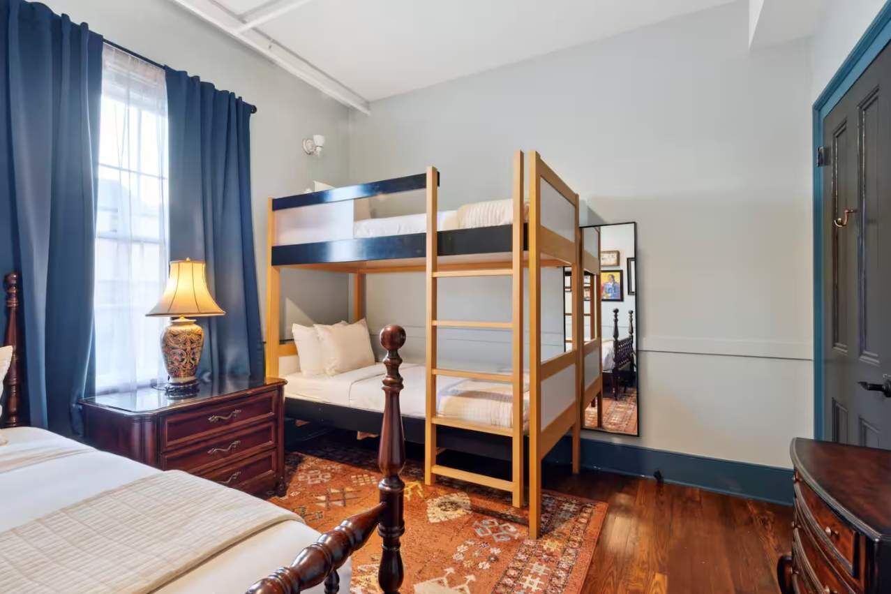 A bedroom with a bunk bed, a bedside table with a lamp, a dresser, and a patterned rug.