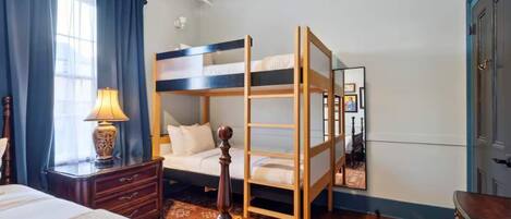 A bedroom with a bunk bed, a bedside table with a lamp, a dresser, and a patterned rug.
