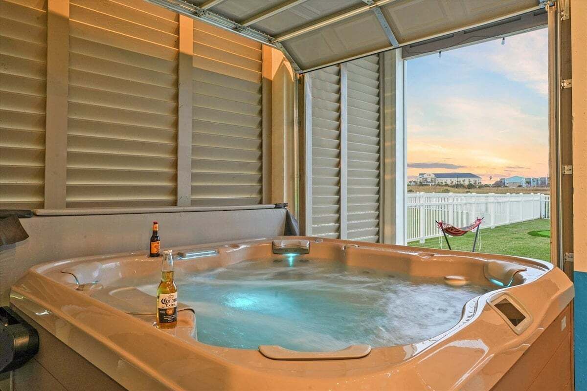 Uma banheira de hidromassagem com uma garrafa de Corona, uma rede e vista para a cidade através de uma grande janela.
