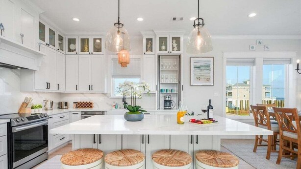 Una cocina moderna con armarios blancos, una isla central con taburetes e iluminación colgante.