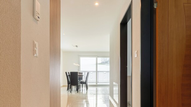 A clean, modern hallway with a wooden door, a dining area with chairs, and a large window with a view. - Cozy 2-bedroom apartment in charming Safenwil with WiFi (Safenwil)