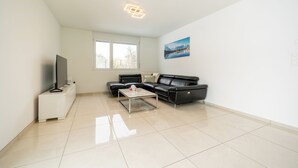 A modern living room with a black leather sofa, a glass coffee table, a flat-screen TV on a white cabinet, and a painting of mountains on the wall. - Cozy 2-bedroom apartment in charming Safenwil with WiFi (Safenwil)