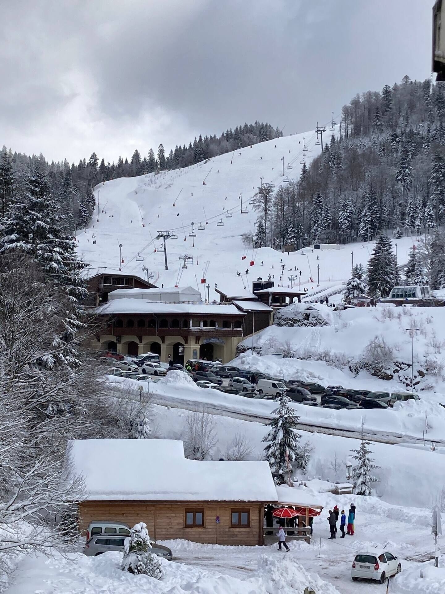 Une station de ski avec un bâtiment qui ressemble à un chalet ou à un restaurant, un espace de stationnement et un télésiège en arrière-plan.