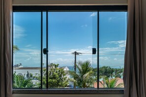 A window with a view of a residential area, including houses and palm trees. - Suíte 7 Ala pôr sol Residencial Solavir (Bombinhas)