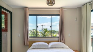 Ein Schlafzimmer mit großem Fenster, einem Bett mit weißer Bettwäsche und einem hölzernen Kopfteil.