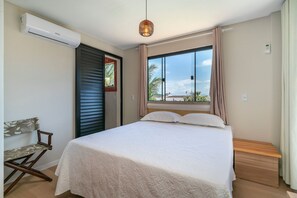 A bedroom with a bed, a chair, an air conditioning unit, a window with curtains, and a view of the outdoors. - Suíte 7 Ala pôr sol Residencial Solavir (Bombinhas)