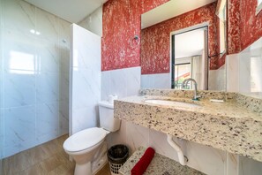 A bathroom with a white toilet, a sink with a granite countertop, and a red towel on the floor. - Suíte 7 Ala pôr sol Residencial Solavir (Bombinhas)