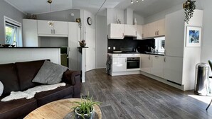 A modern kitchen with white cabinets, a stove, and a sink. There's a dining area with a brown leather couch and a round wooden table with a plant.