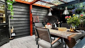 A covered patio area with a table set for dining, surrounded by chairs, and a hanging plant.