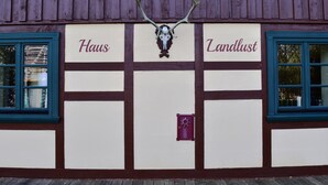 Ein Gebäude mit der Aufschrift "Haus" und "Landlust" an der Fassade, einem aufgehängten Schädel mit Geweihen über dem Eingang und einem kleinen, violetten Briefkasten.