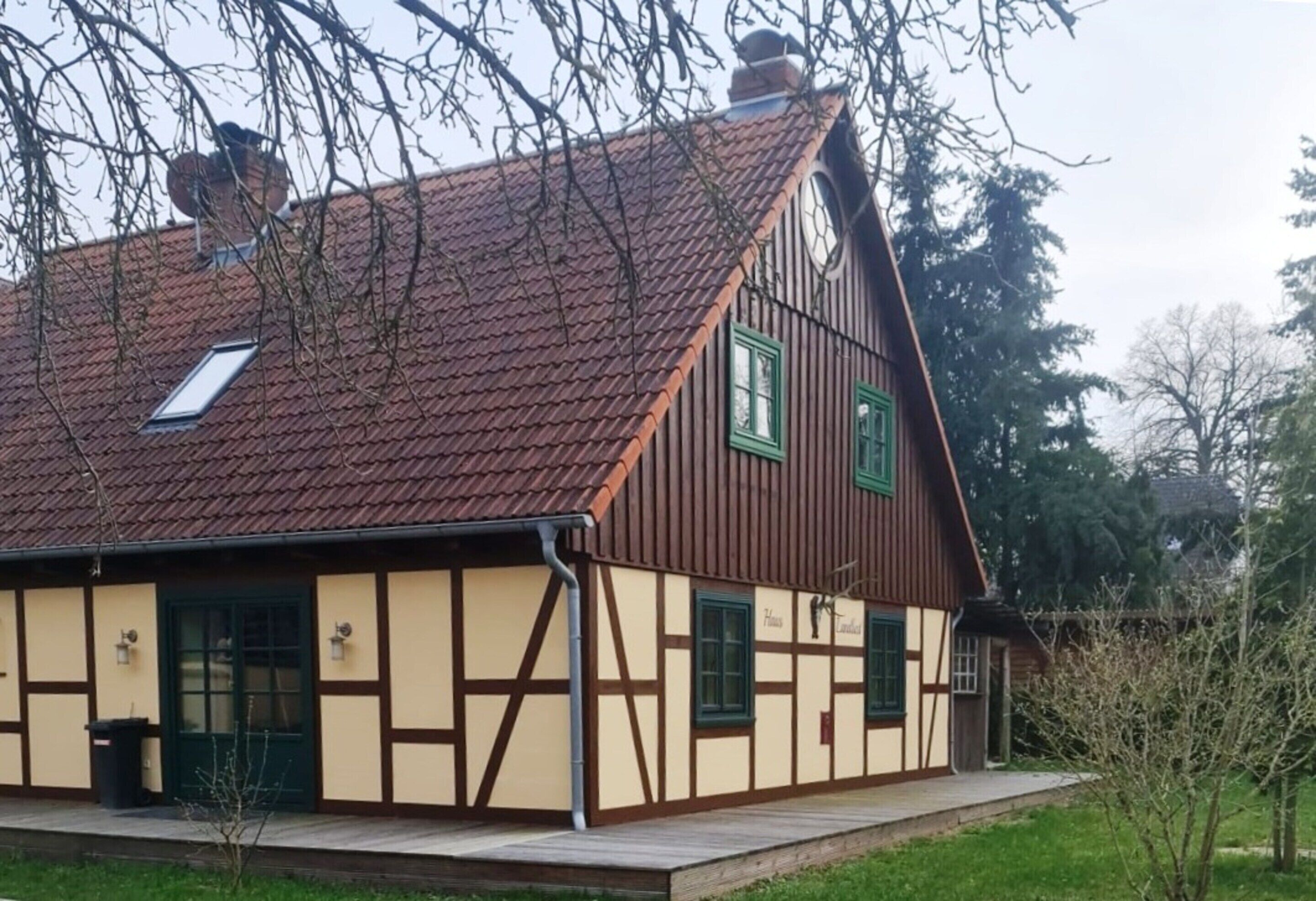 Une maison traditionnelle à colombages, dotée d’un toit en pente, d’une cheminée visible et d’une petite fenêtre à cadre vert.