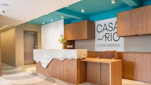 A reception desk with a wooden finish, a white counter, and a sign reading "CASA RIC COPACABANA". - Cosy a few Steps From Copacabana Beach Q16 (Rio de Janeiro)