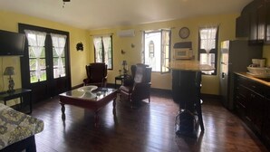 Un ampio soggiorno con pavimento in legno, una ventola a soffitto, una televisione e un'area pranzo con tavolo e sedie.