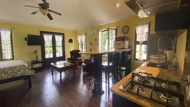 Un ambiente compatto con un letto, un'area pranzo, una cucina completa di piano cottura a gas e una ventola a soffitto.