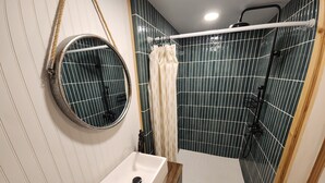 Une salle de bain avec un miroir rond, un lavabo, une douche avec un rideau et un mur carrelé.