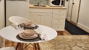 Une cuisine compacte avec un réfrigérateur blanc, un four à micro-ondes et un évier. On y trouve une table à manger, mise pour deux personnes, avec des assiettes et des verres.
