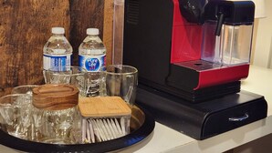 Une machine à café, un plateau avec des verres, deux bouteilles d’eau et un porte-serviettes en bois.
