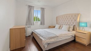 Un dormitorio con una cama grande, mesitas de noche de madera, una lámpara de noche y una ventana con cortinas.
