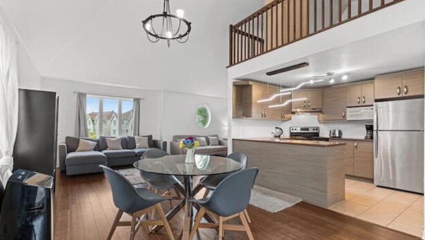 Una cocina moderna con electrodomésticos de acero inoxidable, un comedor con mesa de vidrio y una sala de estar con sofá y vistas al exterior.