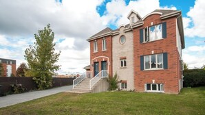 A two-story brick house with a front entrance, a staircase, and a small front yard. - Lovely 2-bedroom Apt. in DIX30 close to DT (Brossard)