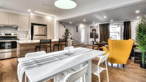 A modern kitchen with stainless steel appliances, a dining area with a white table and chairs, and a bright pendant light. - Lux. 4BR House with Pool near DT (Brossard)