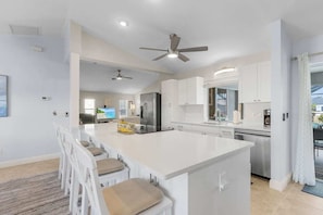 A modern kitchen with a central island, white cabinetry, and ceiling fans.
