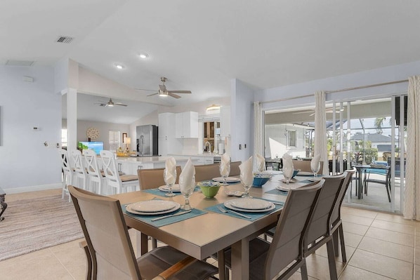 A dining area with a table set for four, a kitchen in the background, and a view of the outdoors.