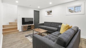 A modern living room with a grey sectional sofa, a wooden coffee table, and a flat-screen TV on a wooden stand. - Elegant 4 bedroom modern house (Brossard)