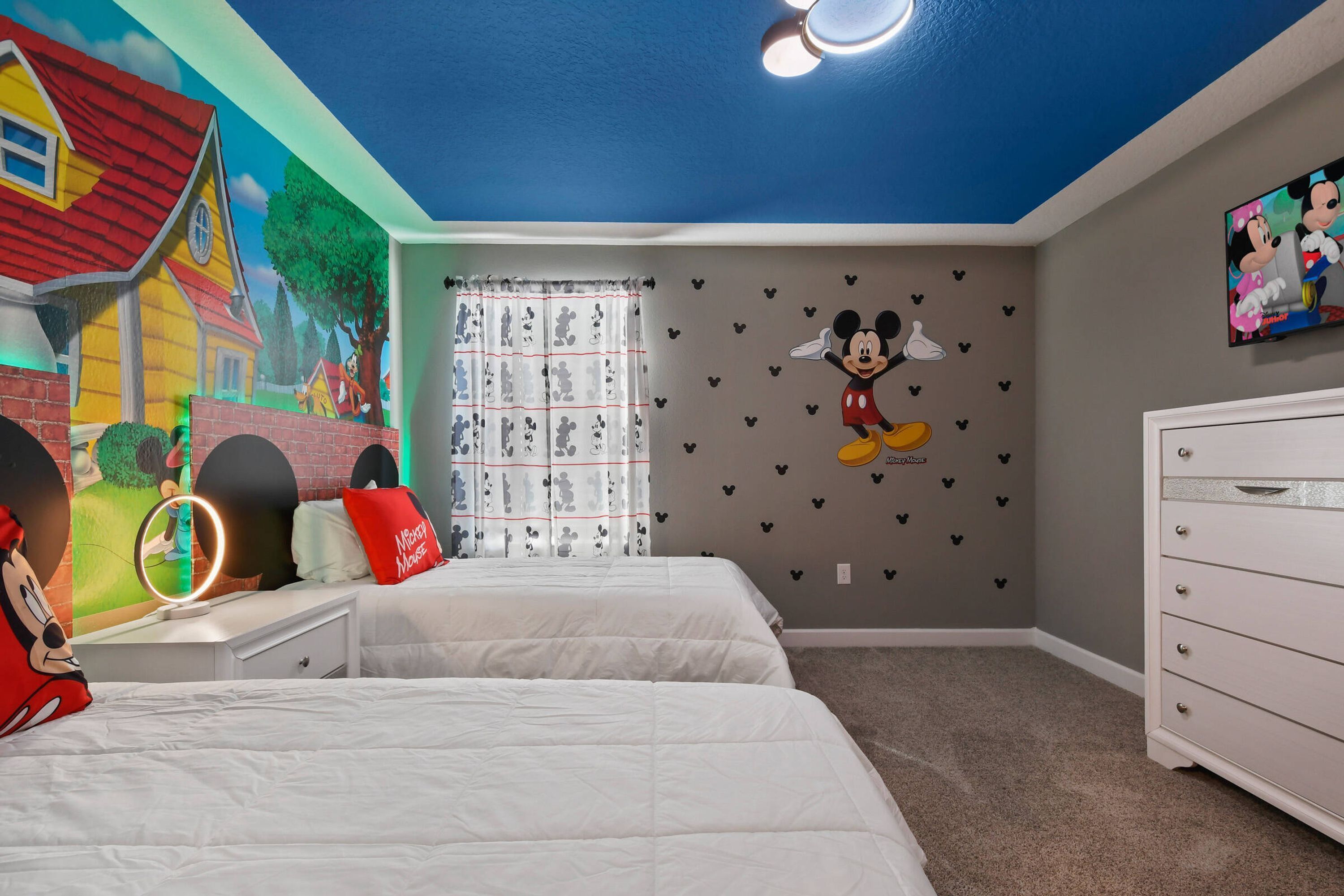 Un dormitorio con dos camas, un adhesivo de pared de Mickey Mouse, una almohada de Mickey Mouse, un cartel de Mickey Mouse y un espejo de Mickey Mouse.