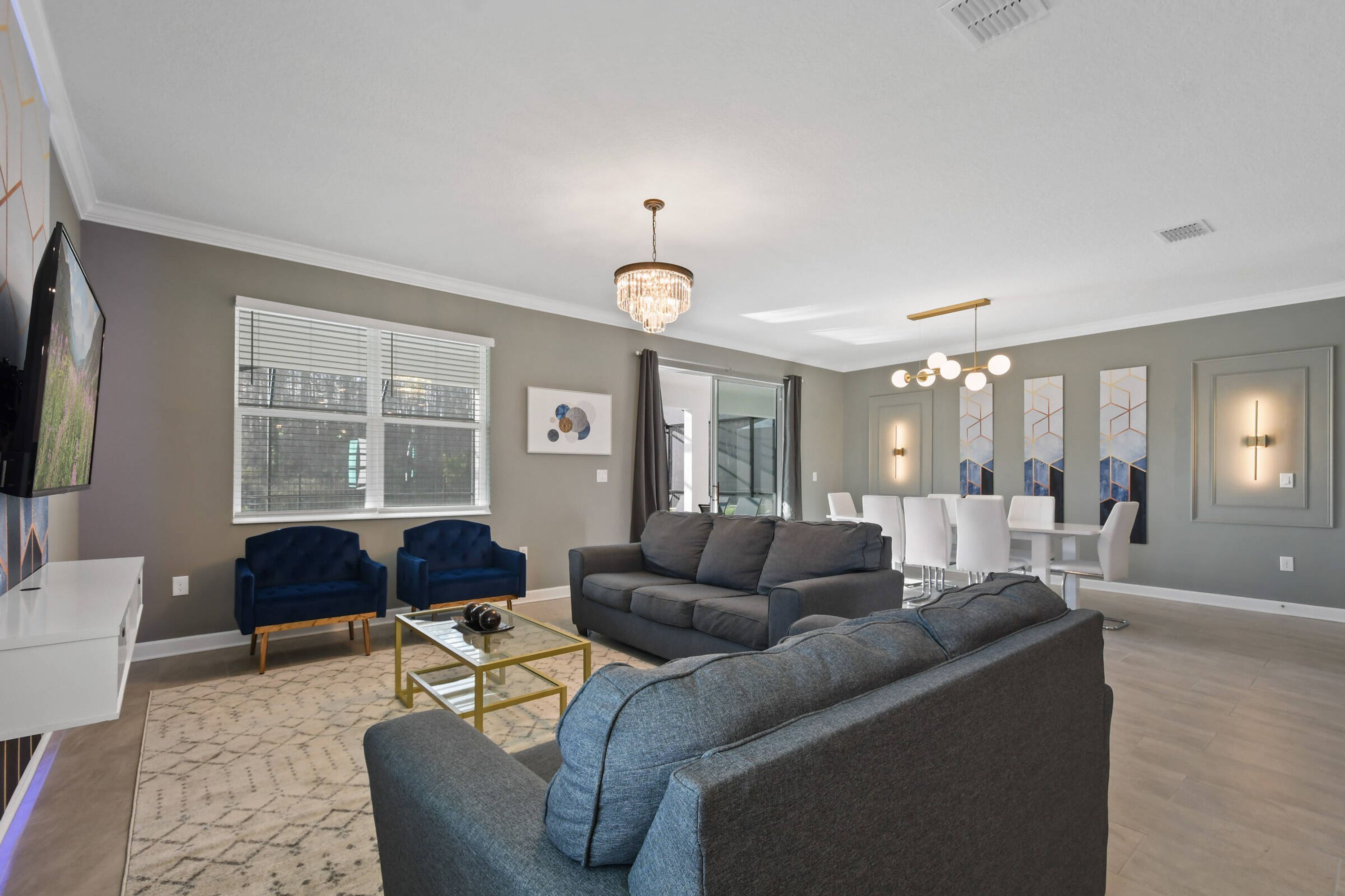 Een moderne woonkamer met een grijze bank, blauwe fauteuils, een salontafel en een kroonluchter.