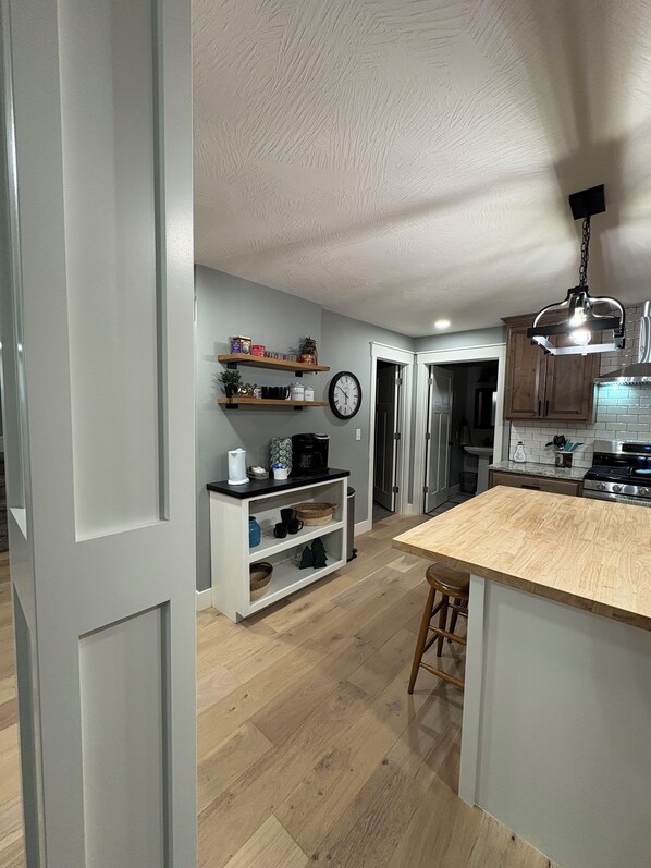 Une cuisine moderne dotée d’un îlot central en bois, d’étagères intégrées et d’un luminaire suspendu.