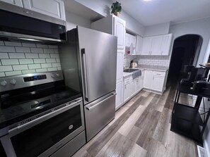 Una cocina moderna con electrodomésticos de acero inoxidable, armarios blancos y un suelo con estampado tipo espiga.