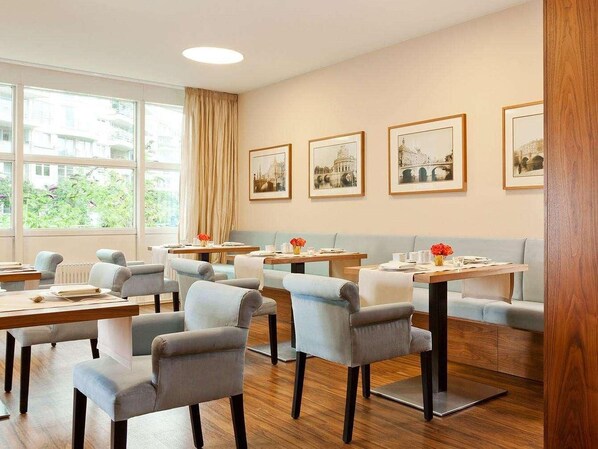 A hotel room with a dining area, multiple tables and chairs, and large windows with curtains. - Abion Villa Suites (Berlin)