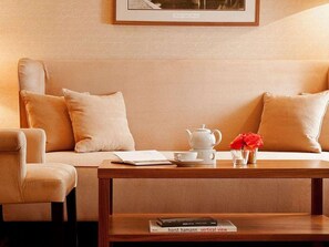A cozy room with a sofa, a wooden coffee table, a teapot, a cup, a book, and a framed picture on the wall. - Abion Villa Suites (Berlin)