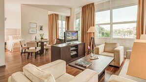 A hotel room with a large window, a television, a dining area, and a sofa. - Abion Villa Suites (Berlin)