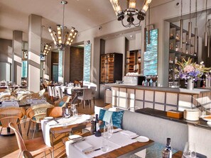A modern restaurant with high ceilings, exposed brick walls, and a central bar area. - Abion Villa Suites (Berlin)