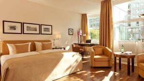 A hotel room with a large bed, two armchairs, a desk, and a window with curtains. - Abion Villa Suites (Berlin)