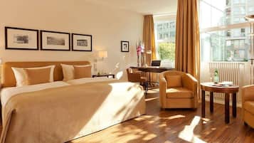 Una habitación de hotel con una cama grande, dos sillones, un escritorio y un ventanal con cortinas.