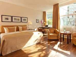 A hotel room with a large bed, two armchairs, a desk, and a window with curtains. - Abion Villa Suites (Berlin)