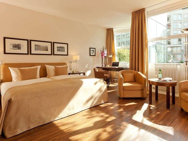 A hotel room with a large bed, two armchairs, a desk, and a window with curtains. - Abion Villa Suites (Berlin)
