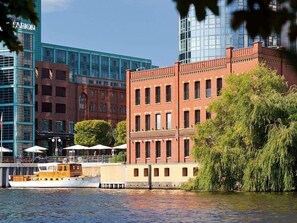 A waterfront building with a brick facade, a glass structure in the background, and a boat docked in front. - Abion Villa Suites (Berlin)