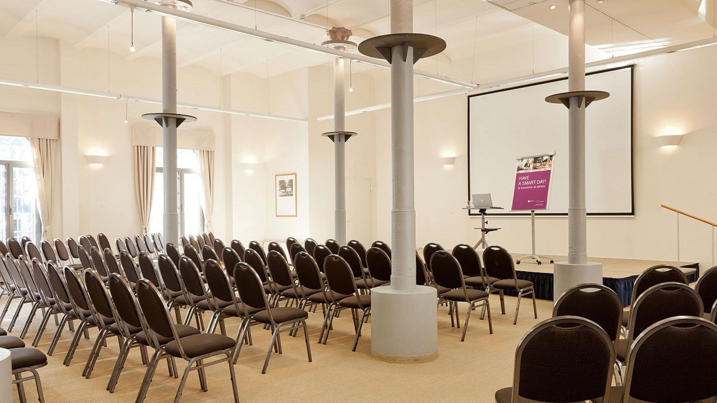 Un salón de conferencias con filas de sillas, un atril y una pantalla grande.