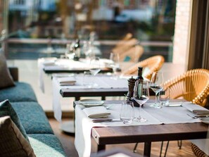 A restaurant with outdoor seating, tables set with wine glasses and plates, and wicker chairs. - Abion Villa Suites (Berlin)