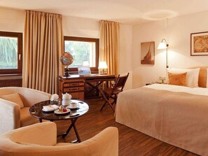 A hotel room with a bed, a desk with a laptop, a chair, a small table with a teapot and cups, and curtains. - Abion Villa Suites (Berlin)