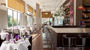 A modern restaurant with a long bar, white tablecloths, and a view of the city. - Abion Villa Suites (Berlin)