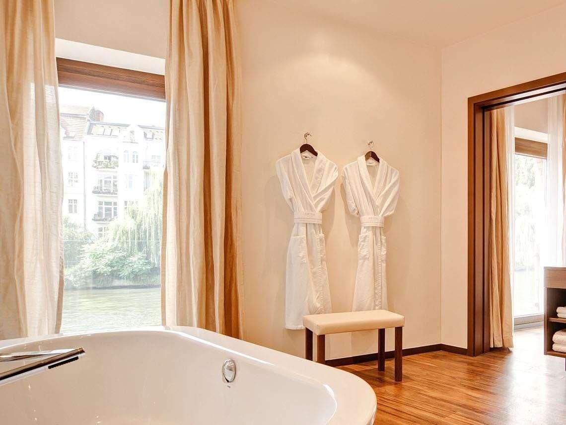 A modern bathroom with a bathtub, a bench, and two white robes hanging on the wall.