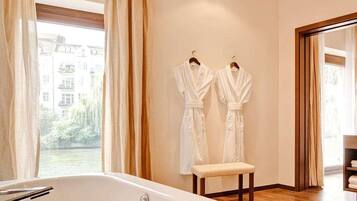 A modern bathroom with a bathtub, a bench, and two white robes hanging on the wall.